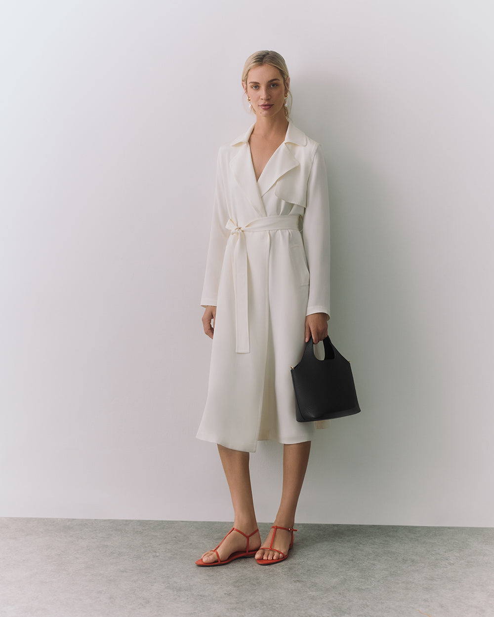 Person in a belted coat holding a handbag.