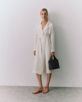 Person in a belted coat holding a handbag.