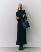 Person standing wearing a long dress and holding a shoulder bag