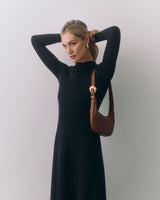 Woman in a dress with hands up, holding a shoulder bag.