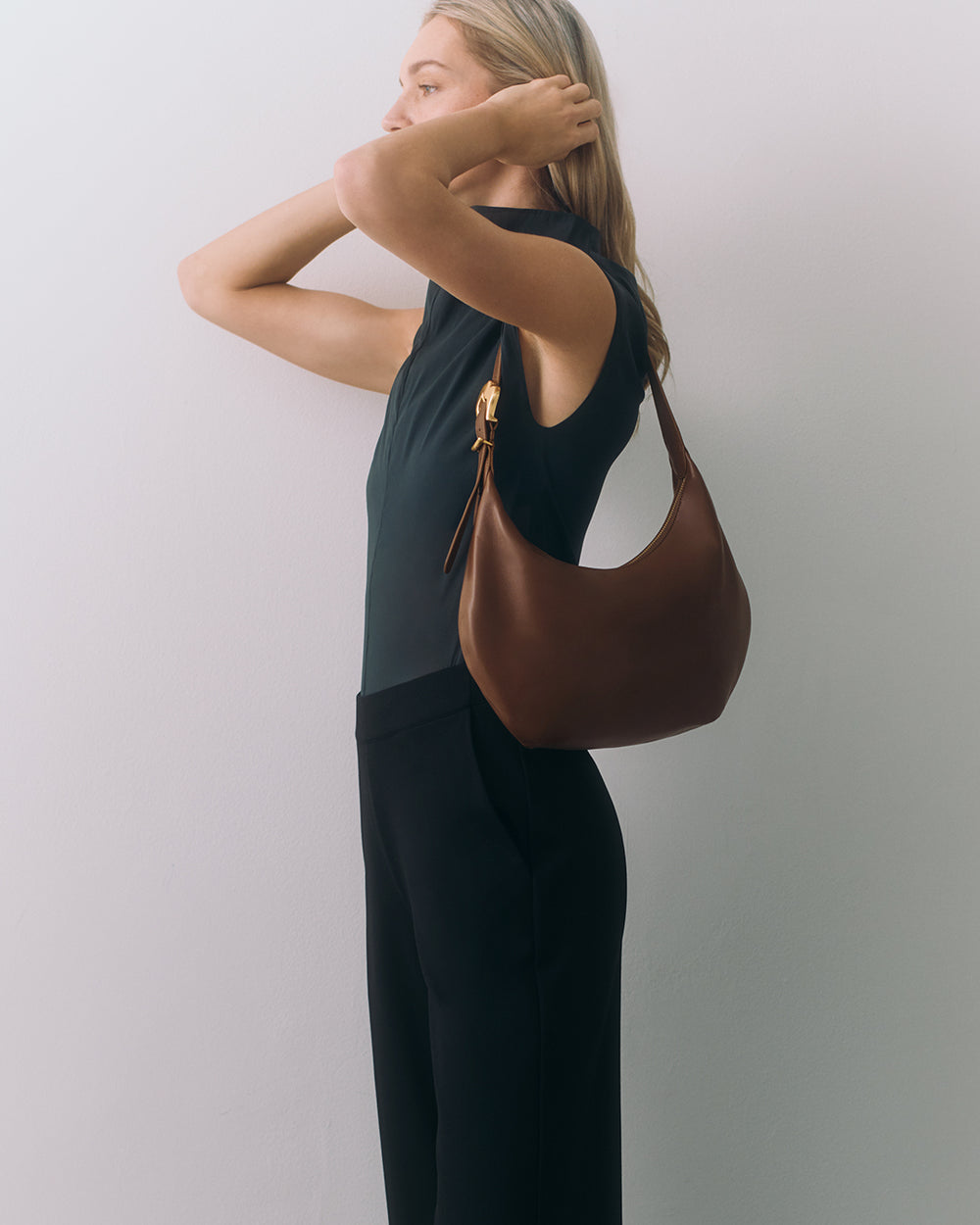 Person holding bag on shoulder, hands touching hair.