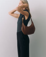 Person holding bag on shoulder, hands touching hair.