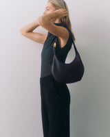 Person in sleeveless top holding a shoulder bag, standing against a plain background.