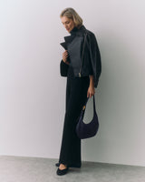 Person in a jacket and pants holding a handbag, standing against a plain background.