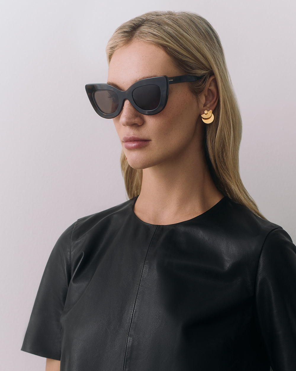 Brisa Sunglasses Woman wearing sunglasses and earrings, dressed in a leather top