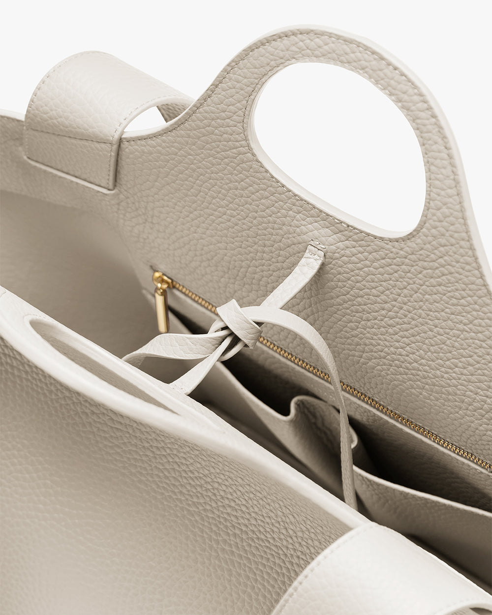 Paloma Tote Open handbag with handles and interior compartments, showing a tied string and a zipper pocket.