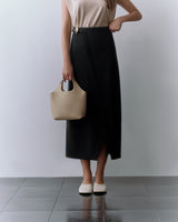 Person holding a handbag, wearing a sleeveless top and long skirt, standing on a tiled floor.