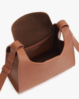 Open handbag with textured surface, standing upright with visible inside and strap attached.