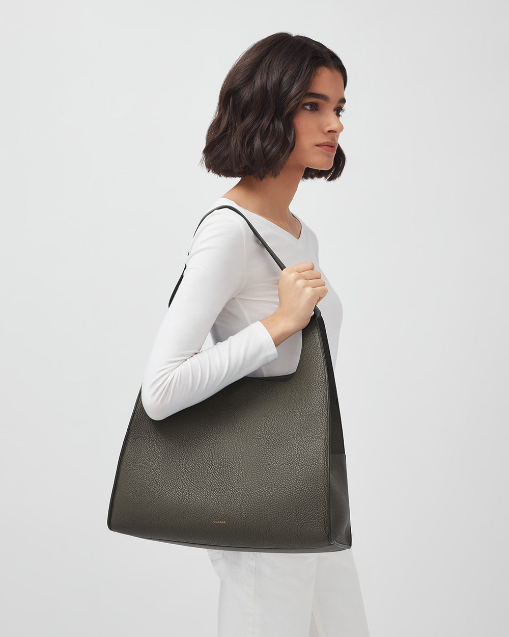 Woman carrying a large tote bag, looking to the side in studio.