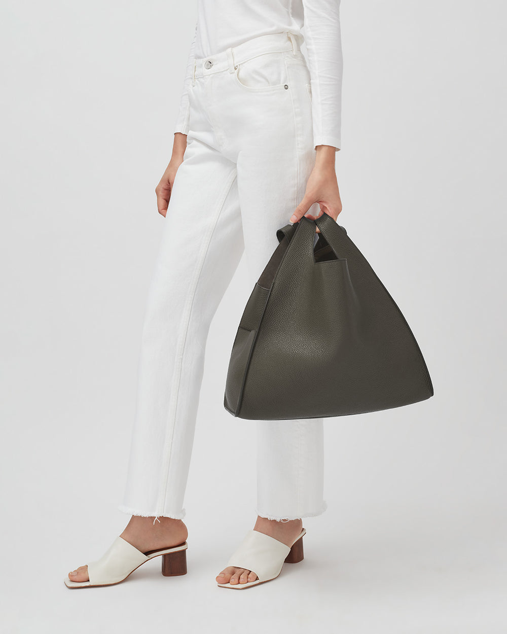 Oversized Double Loop Bag Person standing, holding a large handbag, wearing white pants and heeled sandals.