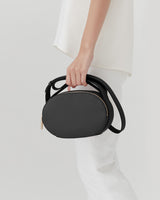 Person holding a small oval handbag by its strap.