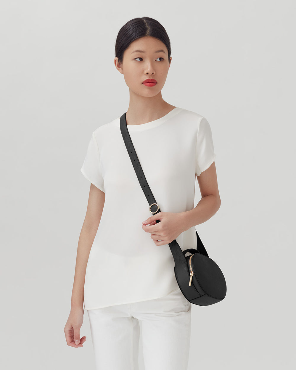 Woman standing with a crossbody bag and looking away.