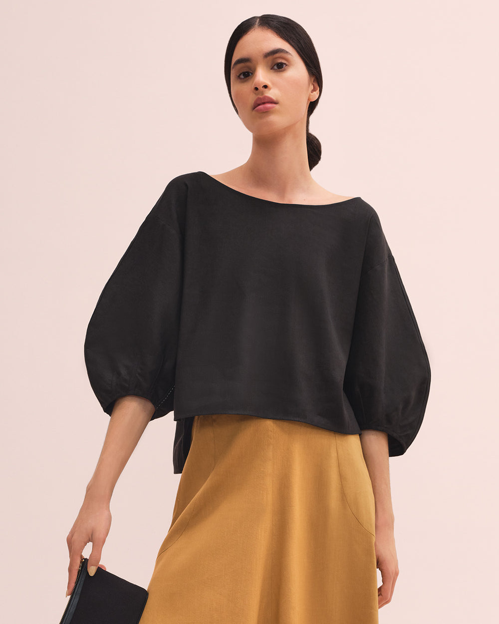 Woman standing with a handbag and wearing a blouse and skirt.