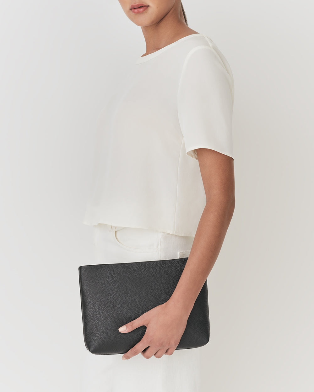 Woman holding a clutch bag, wearing a short-sleeved top and pants.