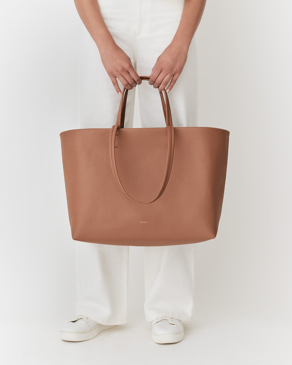 Person holding a large tote bag, standing in white pants and shoes.