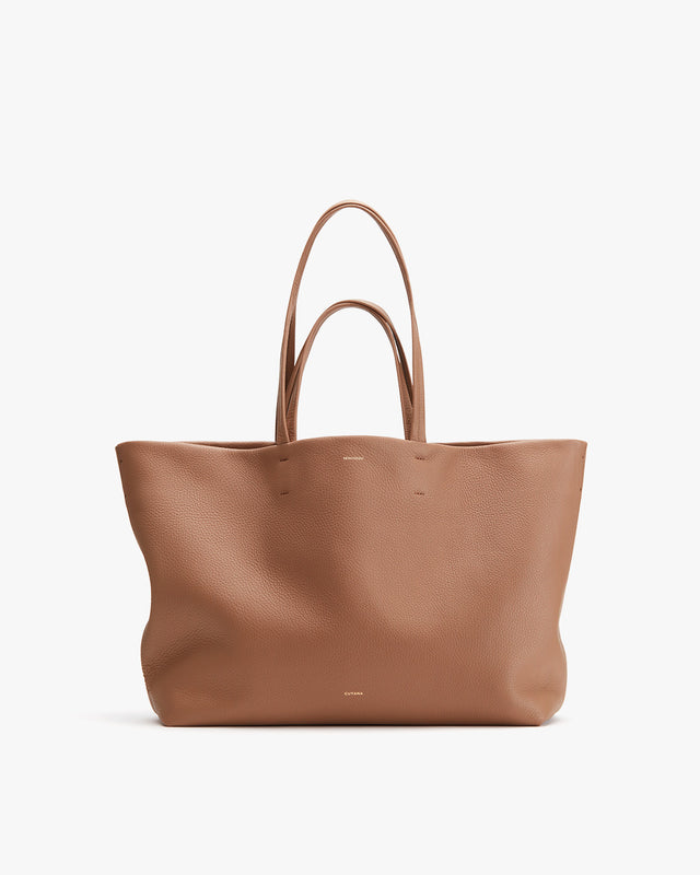 Large leather tote bag with two handles standing upright.