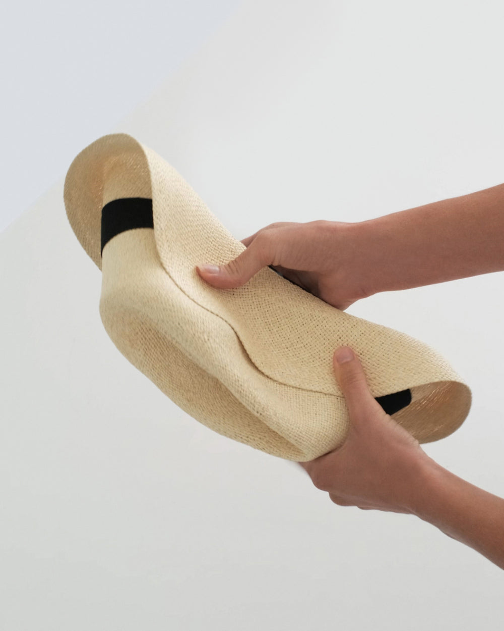 Hands holding a curled brimmed hat against a plain background