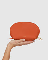 Hand holding a small zippered pouch with a brand logo.