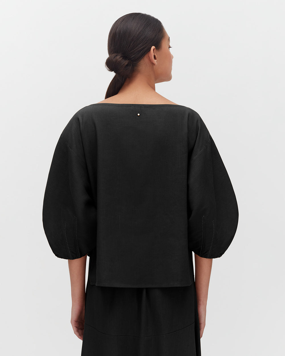 Woman seen from behind, wearing a top with voluminous sleeves and her hair in a bun.