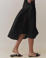 Person walking in a long dress with a high side slit, wearing flat sandals.