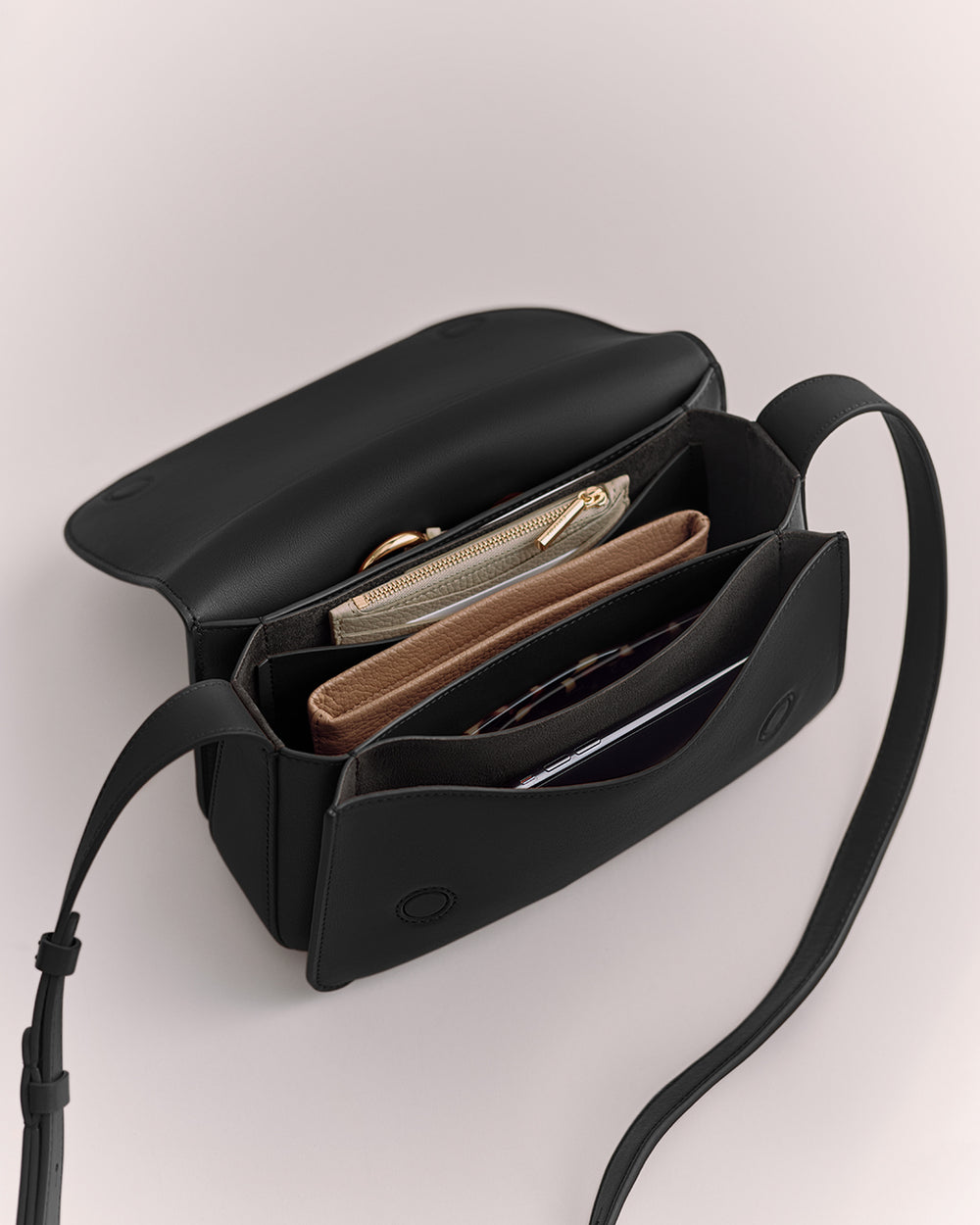 Open handbag with multiple compartments and items inside, featuring a long strap.