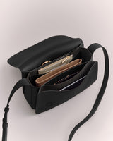 Open handbag with multiple compartments and items inside, featuring a long strap.