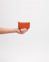 Hand holding a small zippered wallet against a plain background.