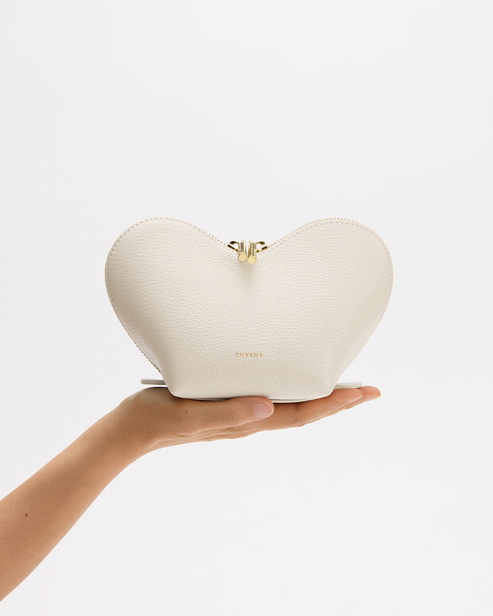 Hand holding heart-shaped pouch against plain background.