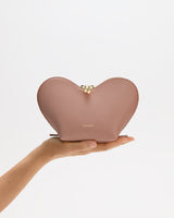 Hand holding heart-shaped pouch against plain background.