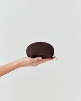 Hand holding a small leather pouch with a zipper.