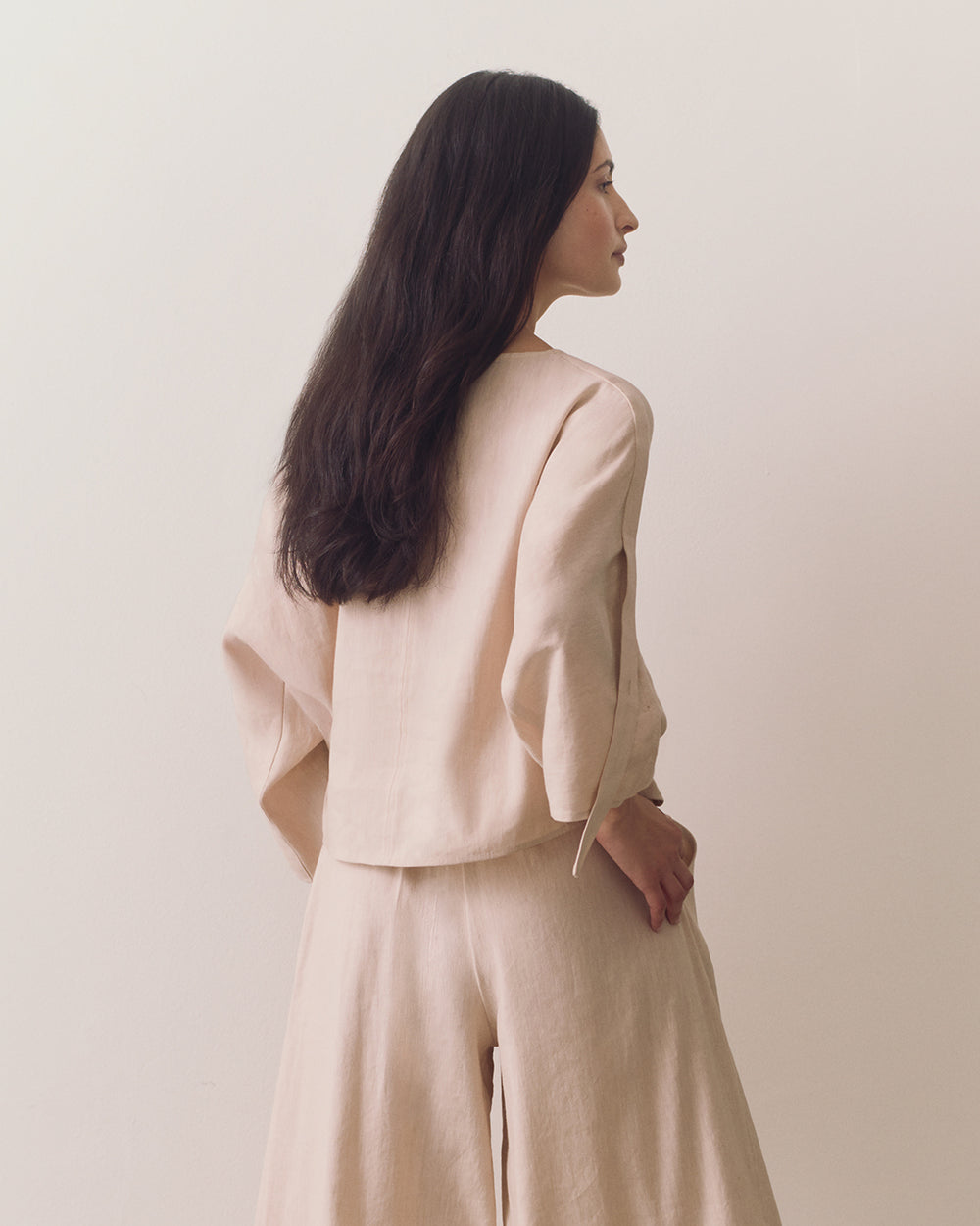 Linen Adjustable Sleeve Top Person wearing loose top and wide-leg pants standing against plain backdrop