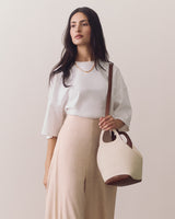 Woman in blouse and pants holding a round handbag over shoulder