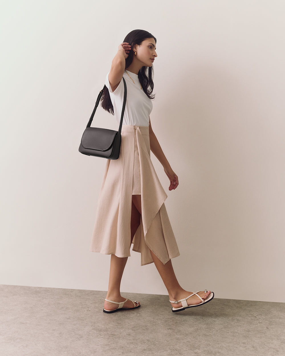 Person walking with shoulder bag and wearing sandals and skirt.