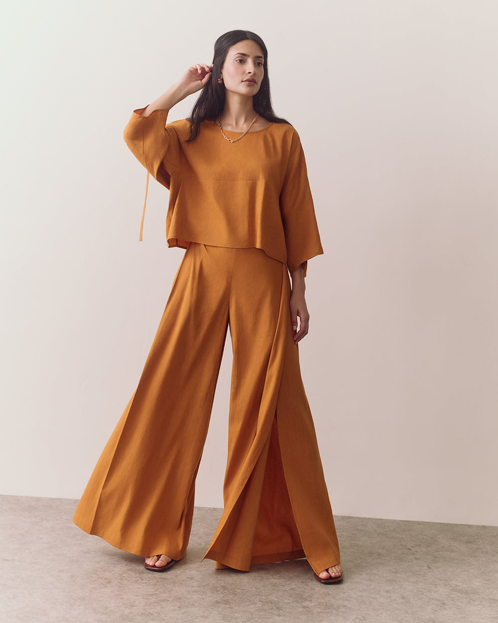 Person wearing a loose top and wide-leg pants, standing on a plain floor.