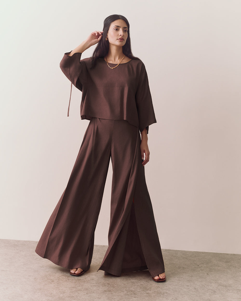 Woman wearing wide-legged pants and loose top, standing on a plain background.