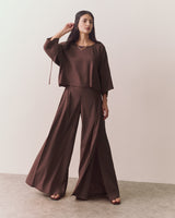 Woman wearing wide-legged pants and loose top, standing on a plain background.