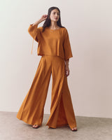 Person wearing a long-sleeve top and wide-leg pants, standing on a plain background.