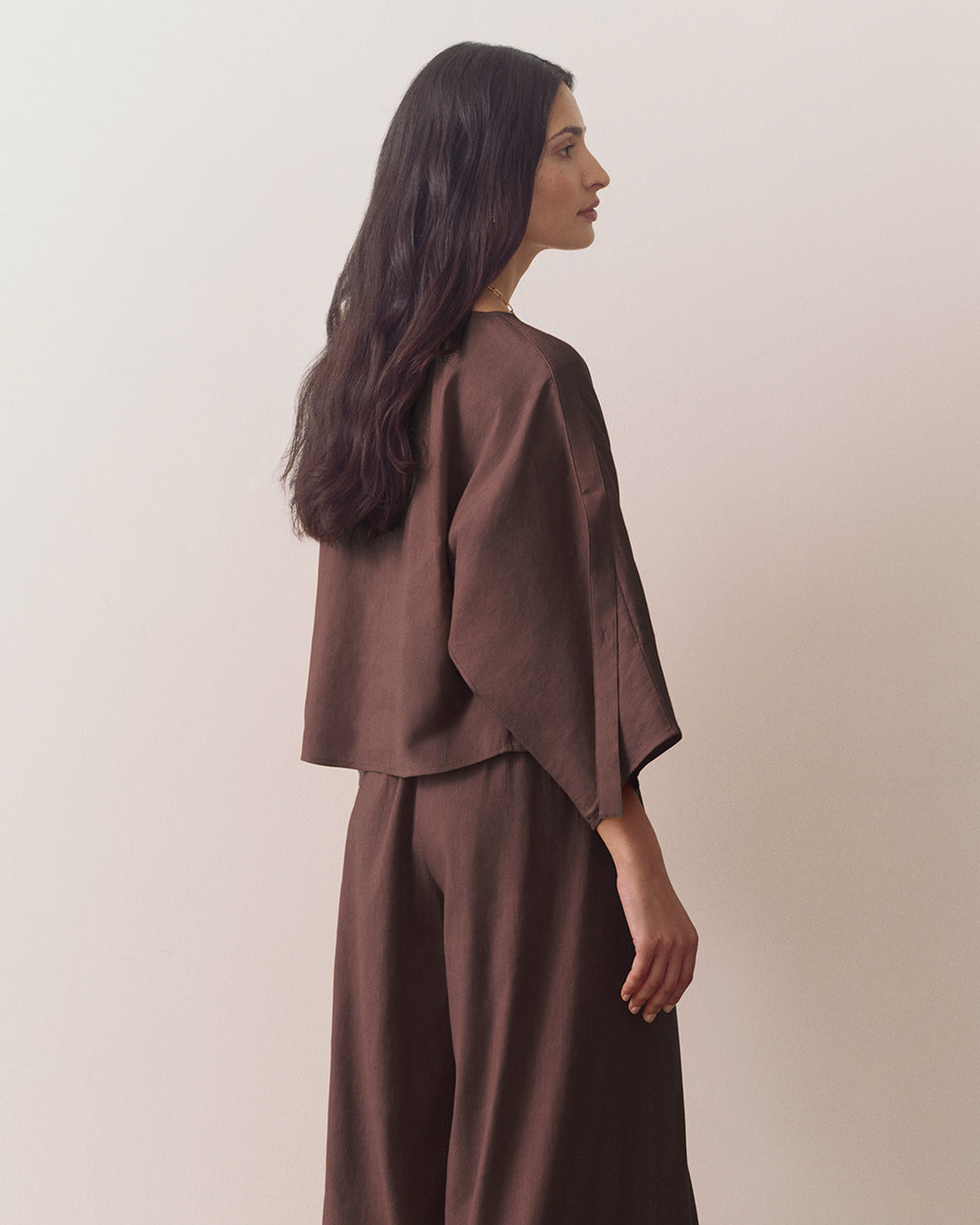 Person wearing loose top and wide-leg pants standing against plain backdrop