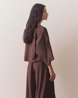 Person wearing loose top and wide-leg pants standing against plain backdrop