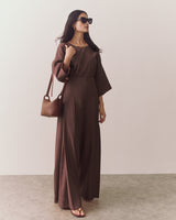 Person wearing loose top and wide-leg pants standing against plain backdrop