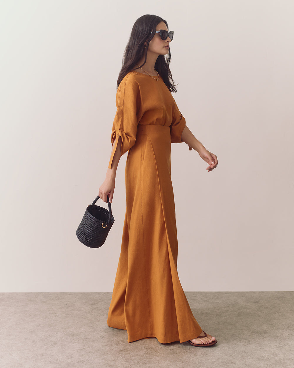 Woman in wide-leg pants holding a small basket bag and wearing sunglasses.