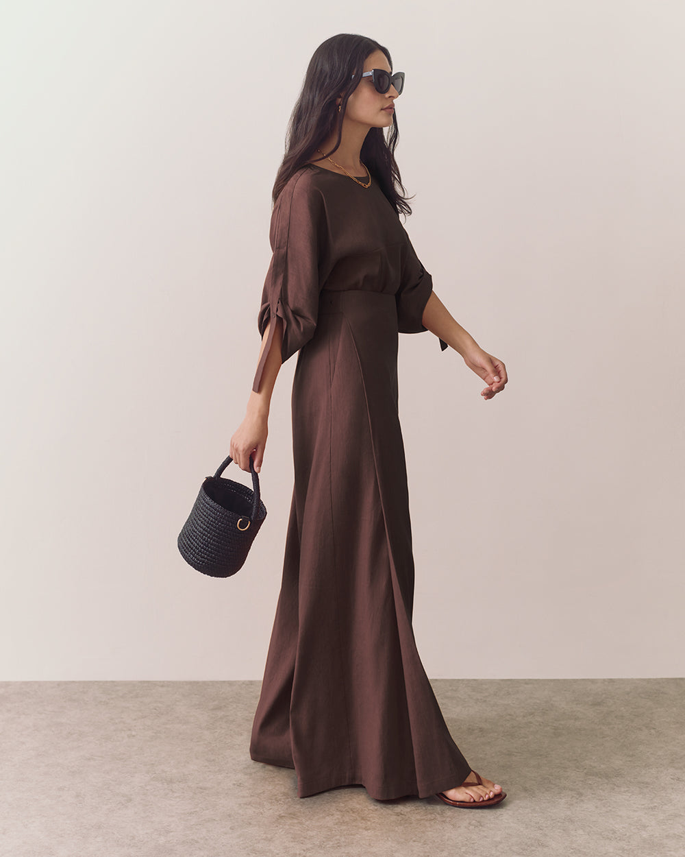 Woman in wide-leg pants holding a small basket bag and wearing sunglasses.