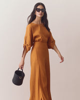 Woman in a blouse and pants, holding small round bag, wearing sunglasses.