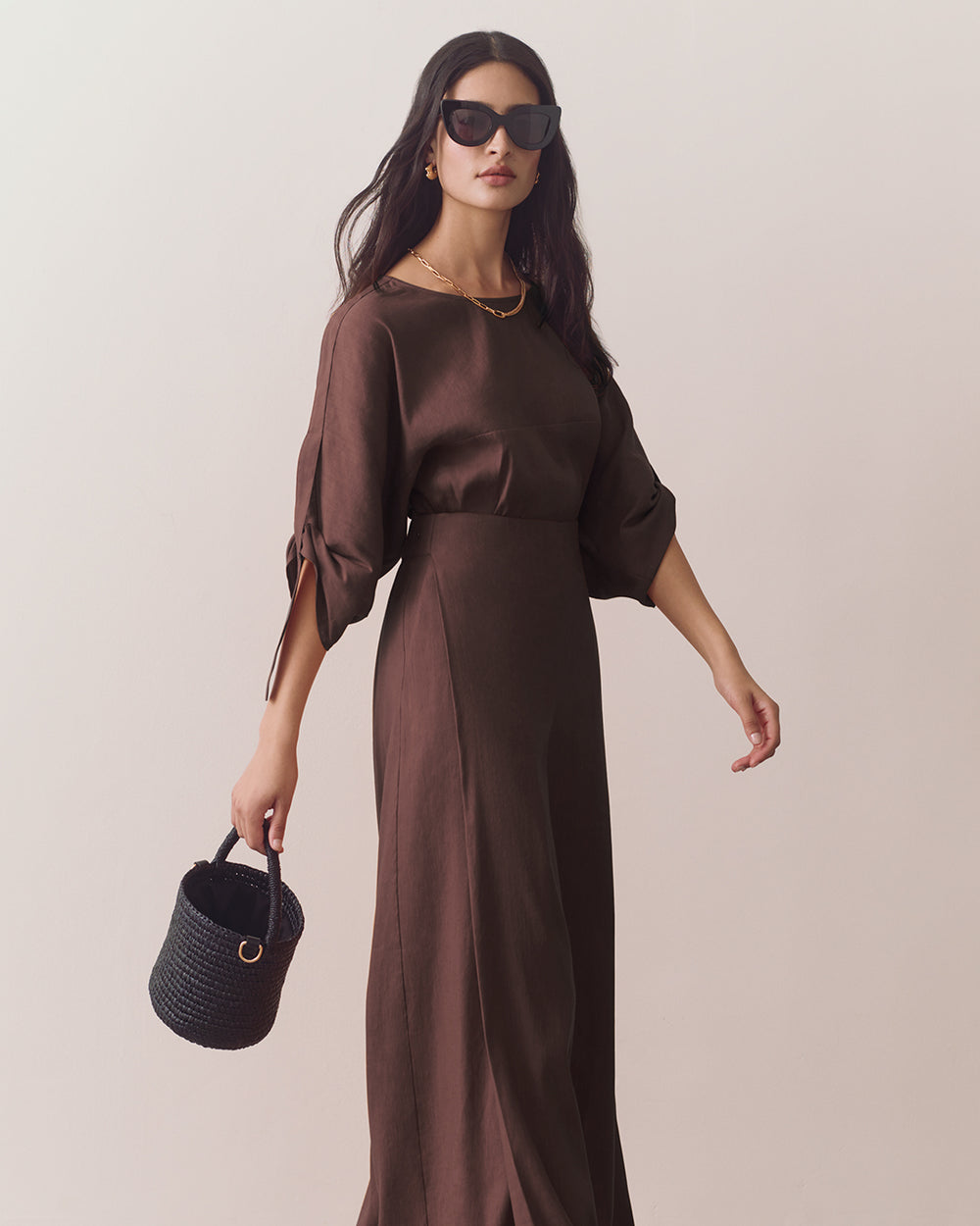 Woman in wide-leg pants holding a small basket bag and wearing sunglasses.