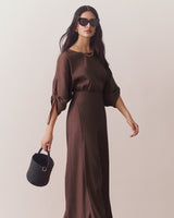 Woman in wide-leg pants holding a small basket bag and wearing sunglasses.