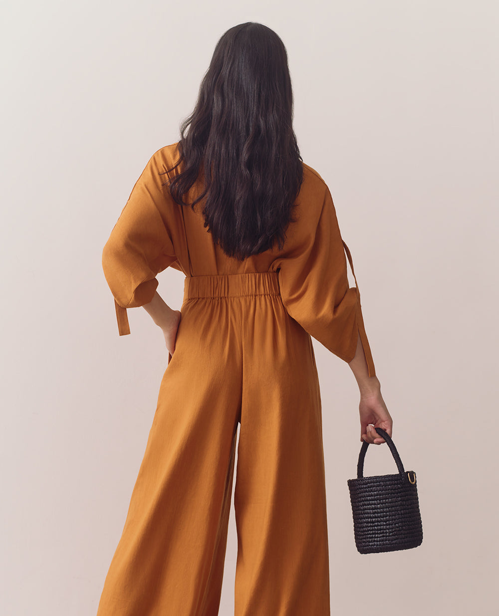 Person wearing loose top and wide-leg pants standing against plain backdrop