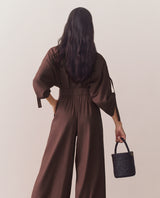 Person wearing loose top and wide-leg pants standing against plain backdrop