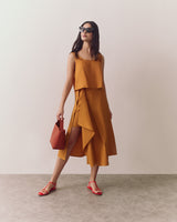 Person in a sleeveless top and flowy skirt, holding a bag, wearing sunglasses and sandals.