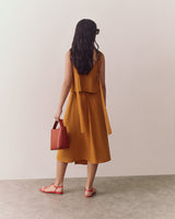 Person in a sleeveless top and flowy skirt holding a small handbag, standing indoors