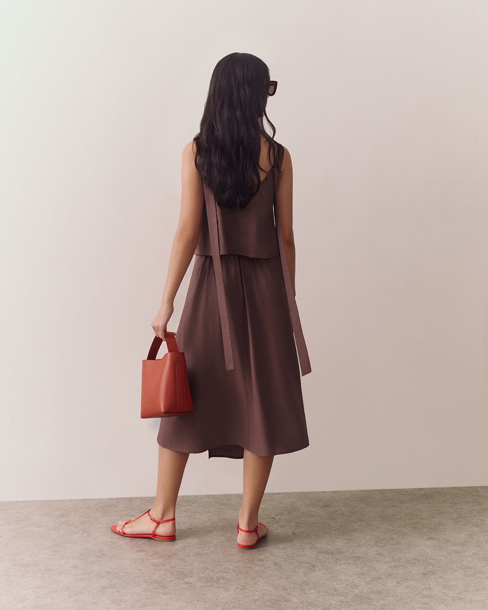 Person in a sleeveless top and flowy skirt holding a small handbag, standing indoors